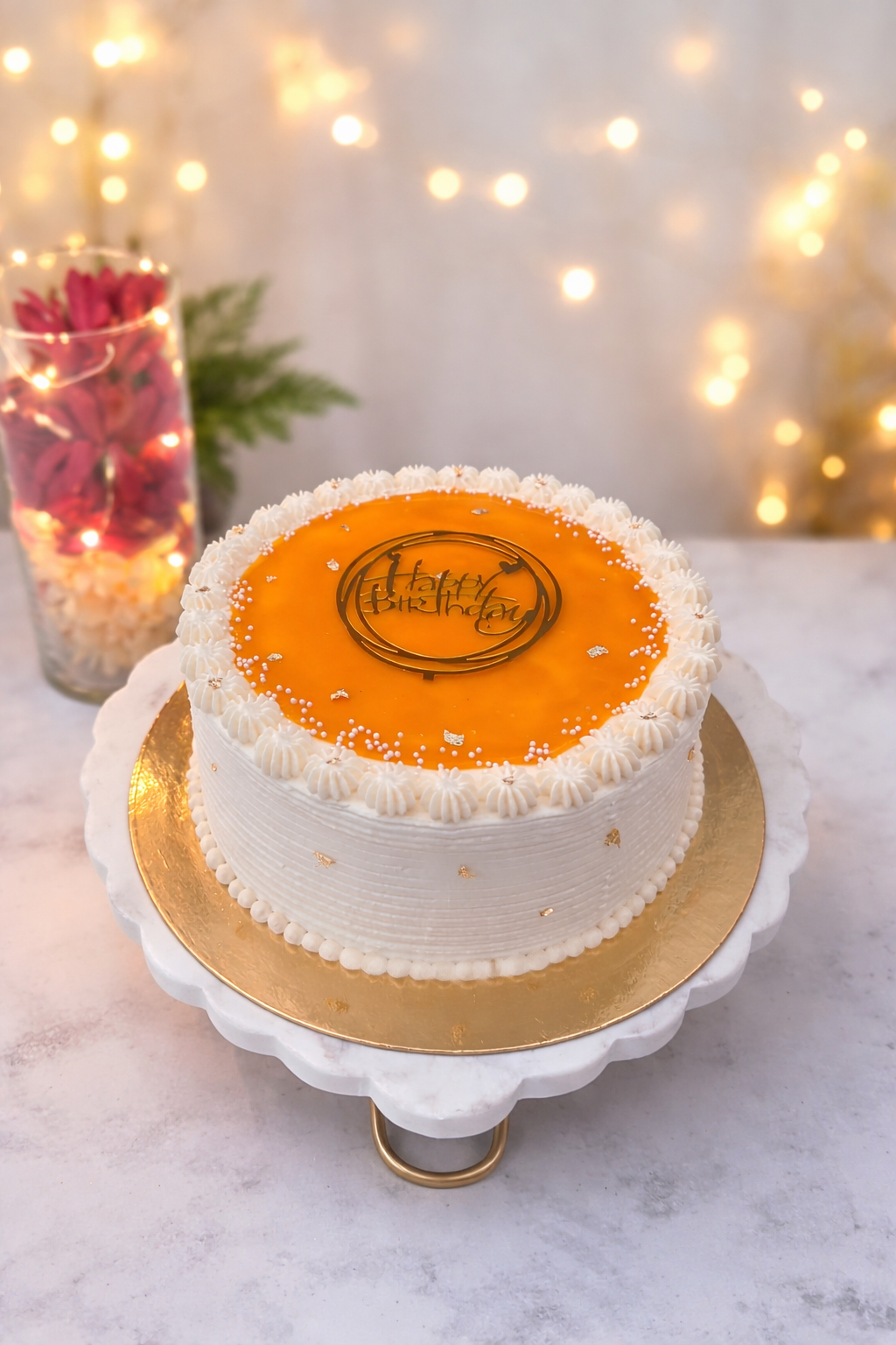 Mango mirror glaze birthday cake on a marble cake stand with warm bokeh lights